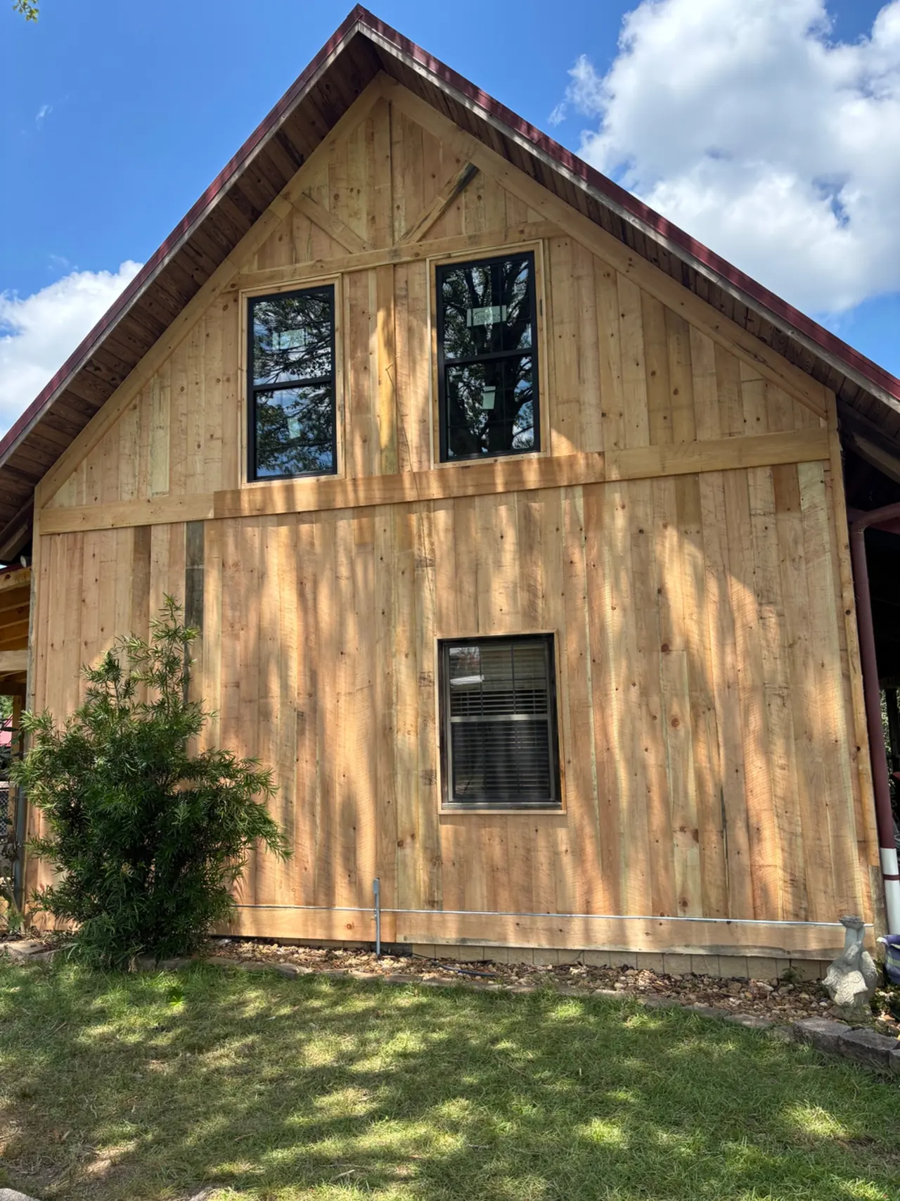 New board-and-batten wood siding with two black-framed windows in the gable of a house with a red metal roof