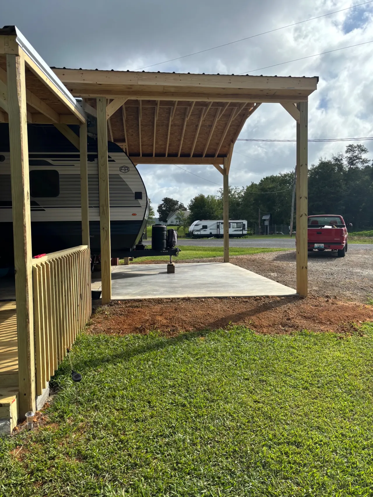 Open-frame carport with posts, angled braces and a metal roof over a concrete pad beside a deck