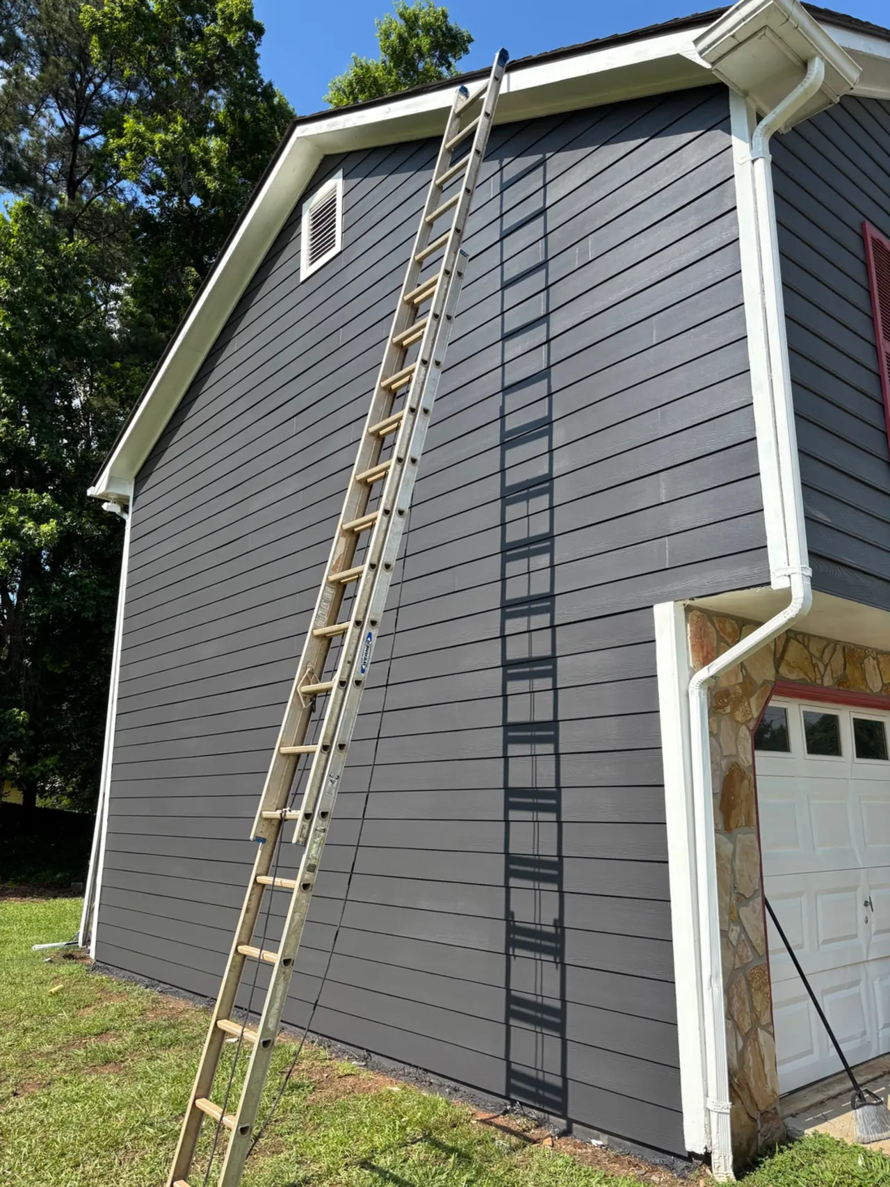 Dark gray lap siding, white trim and gutters beside a stone-faced garage on a two-story house