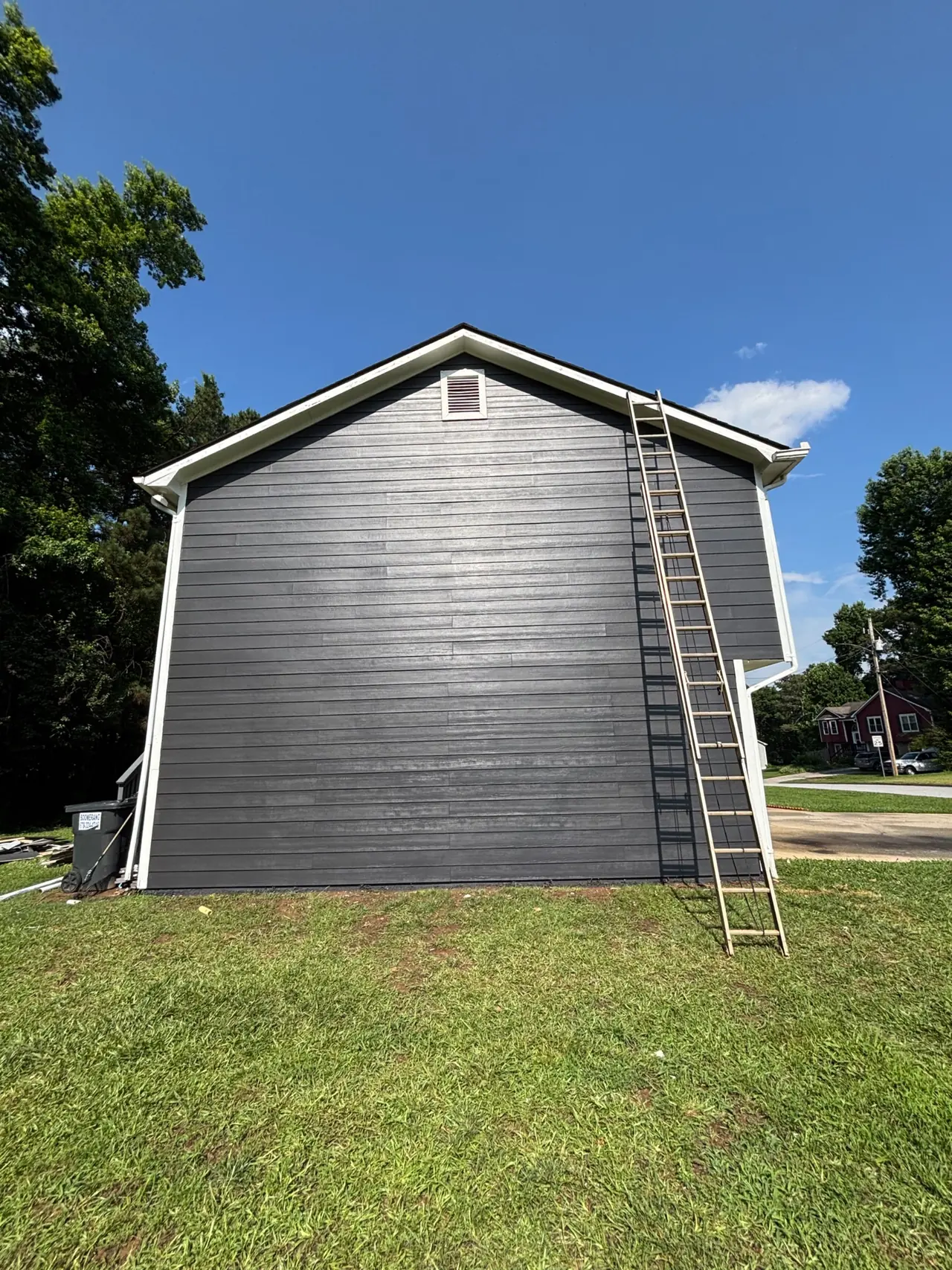Side wall of a two-story house covered in new dark gray lap siding with white trim and a gable vent