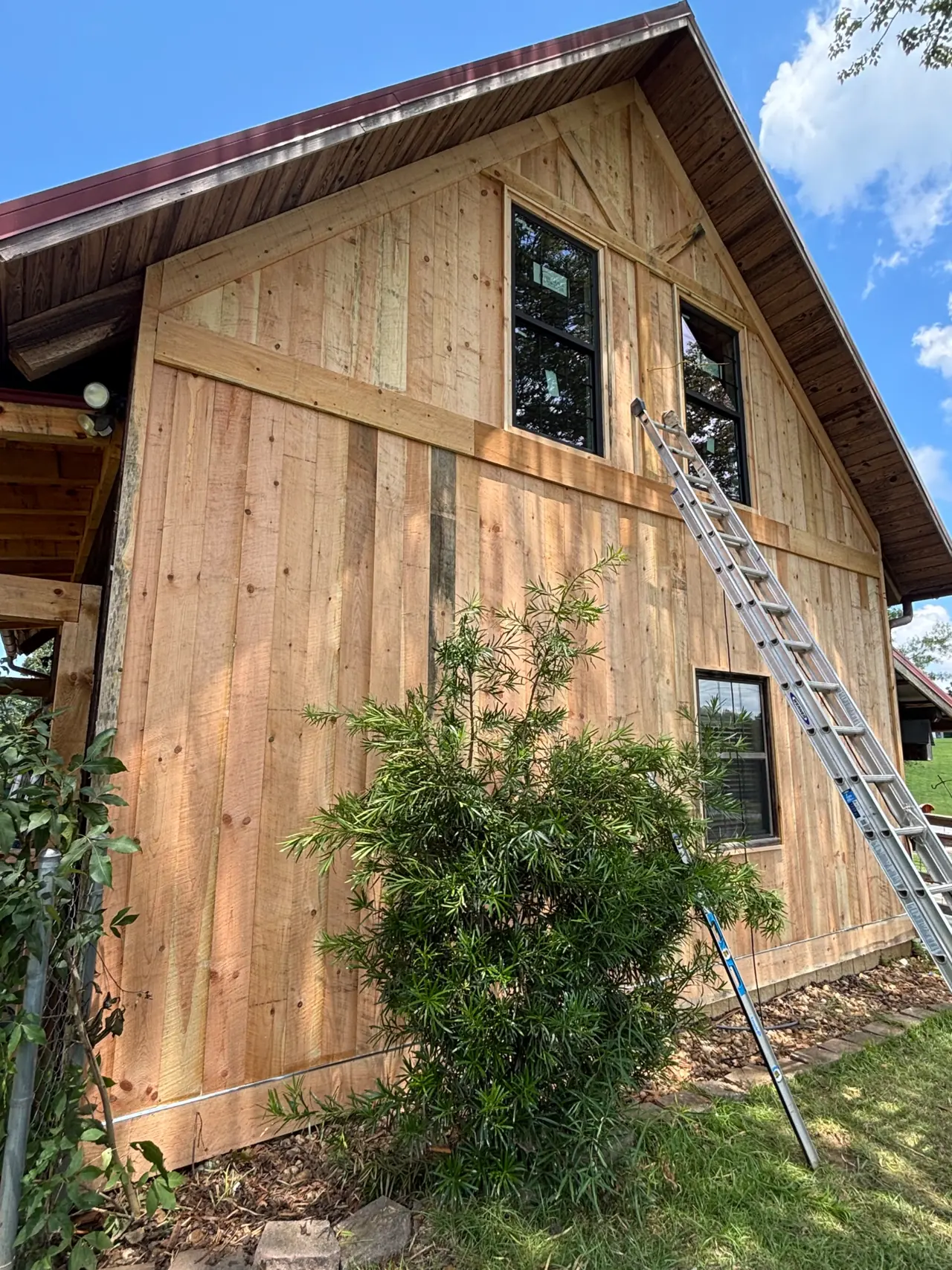 Angled view of new wood board-and-batten siding and gable windows under a red metal roof