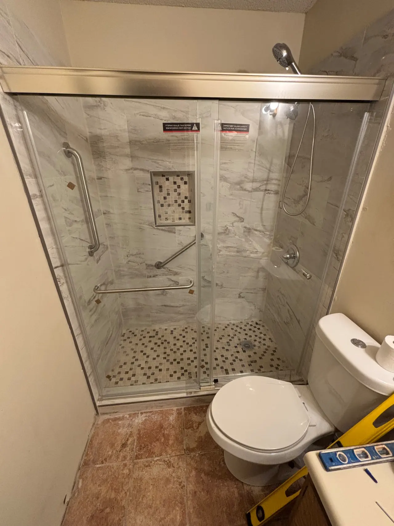 Bathroom shower with a framed sliding glass door and a level resting on the vanity during installation