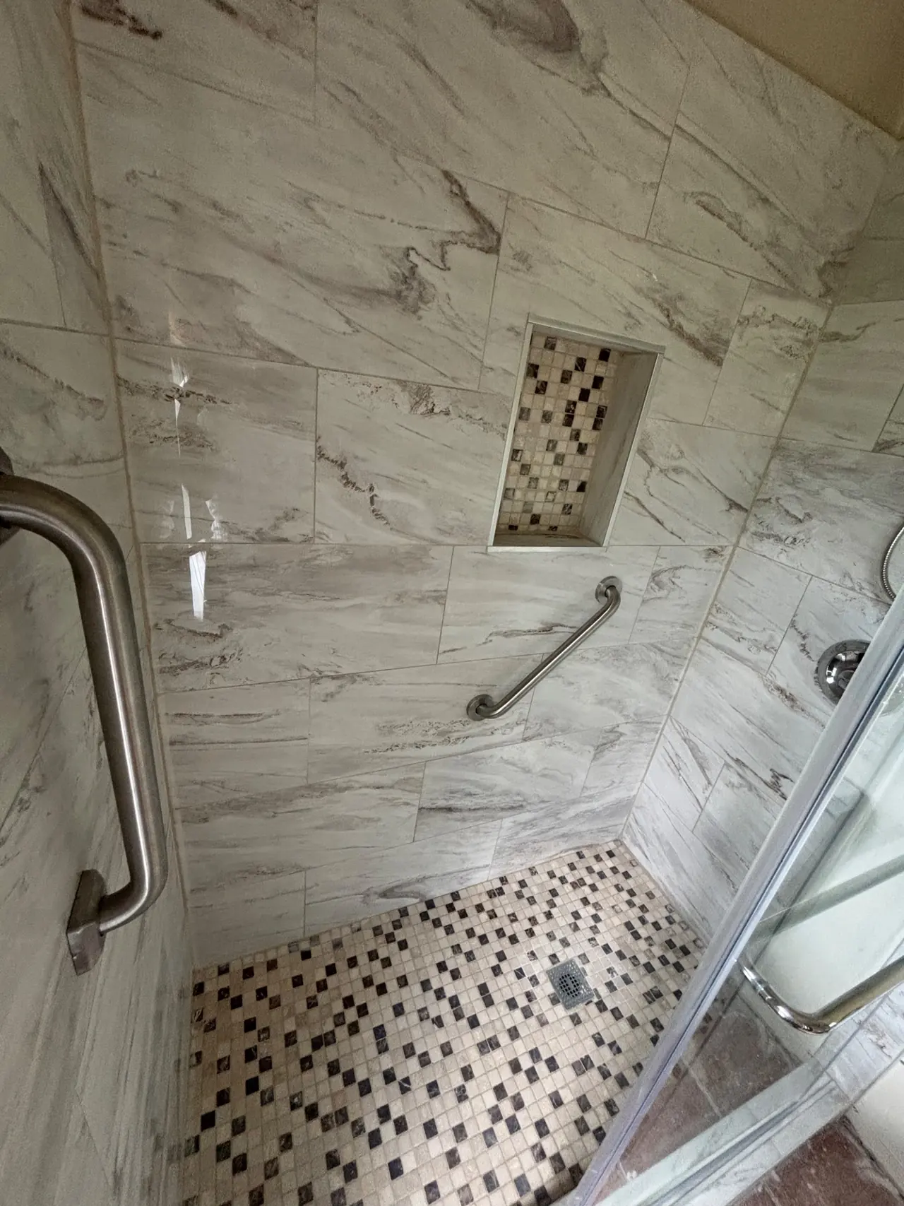 Shower wall with a recessed mosaic-tile niche, grab bars and a brown, tan and black mosaic floor