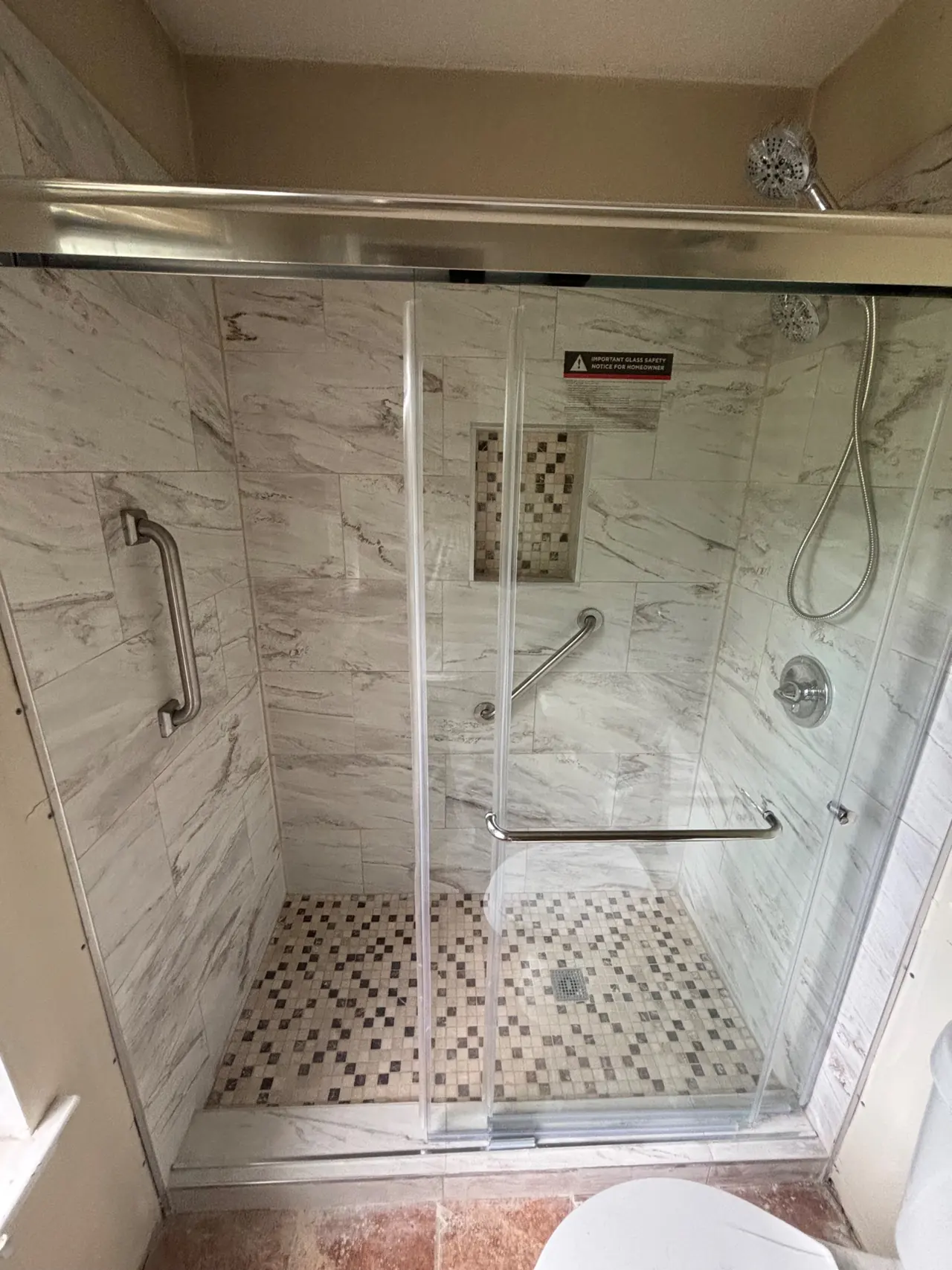 Finished tile shower with a sliding glass door, handheld shower head and grab bars