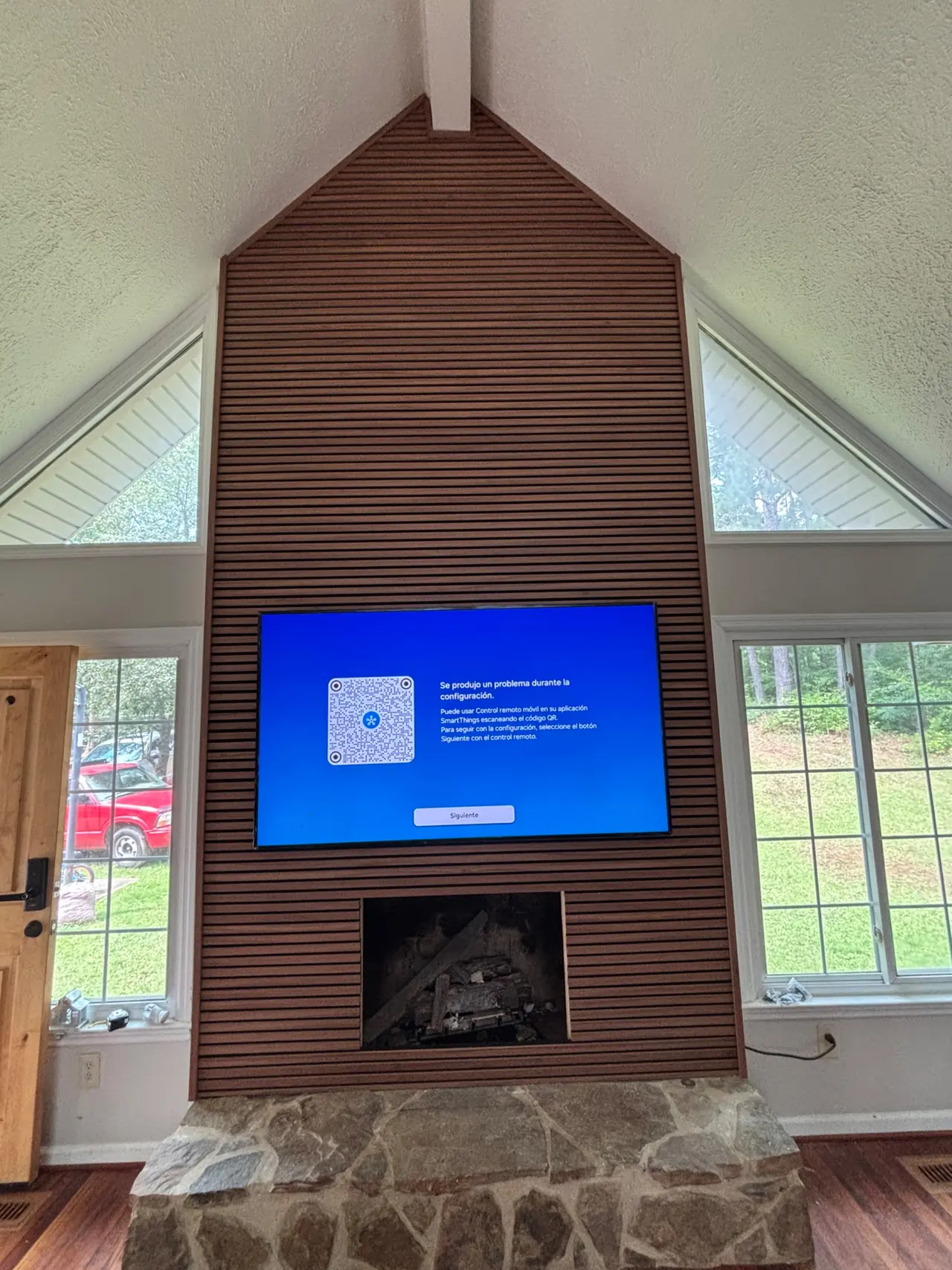 Finished horizontal wood slat feature wall above a stone hearth with a wall-mounted TV between two windows